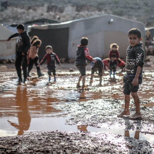 Children playing in muddy water with tents and vehicles in the background, text 'Winter Shelter Appeal Gaza' at the top.