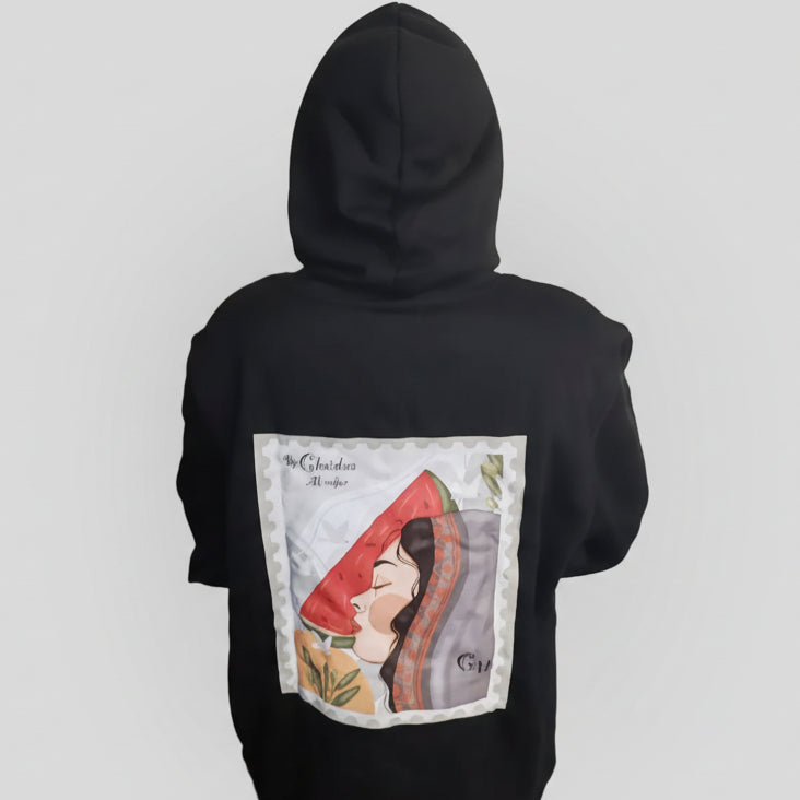 Person wearing a black hoodie with a graphic design on the back, standing in a room with a whiteboard and blue bag.