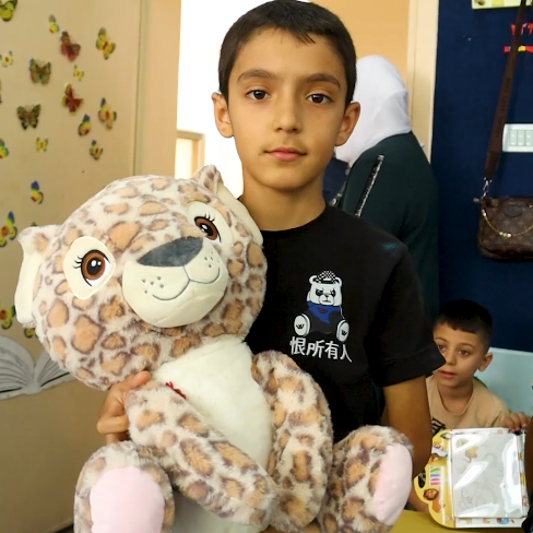 Child holding a stuffed animal in a room with colorful walls and furniture.